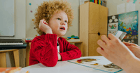 A 4-year-old child in a red sweater gets speech delay therapy from a speech-language pathologist