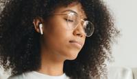 A woman has her headphones in and her eyes closed as she listens to a mental health podcast. Get inspired by listening to these therapy podcasts.