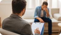 A therapist faces his distressed client. As he writes his session notes he also looks at the client and uses self-disclosure in therapy to show empathy and understanding for the client. There are many benefits and risks to self-disclosure in therapy. In this article, we share examples and ethical considerations for therapist self-disclosure.