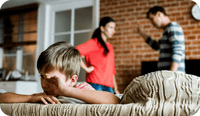 A family, two adults and one child, are in a room, the two adults are engaged in an argument while the child faces away from them on the couch, hand covering his face. Family therapy interventions can strengthen a variety of relationships. This article shares family therapy techniques you can use with clients.