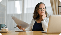 A therapist looks at her laptop and holds some paperwork while wondering how to get a raise in her insurance reimbursement rate.