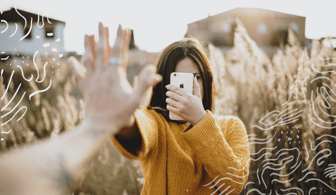 Girl covering face with iPhone and holding up hand