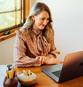 A woman sits at a desk smiling at her latptop.