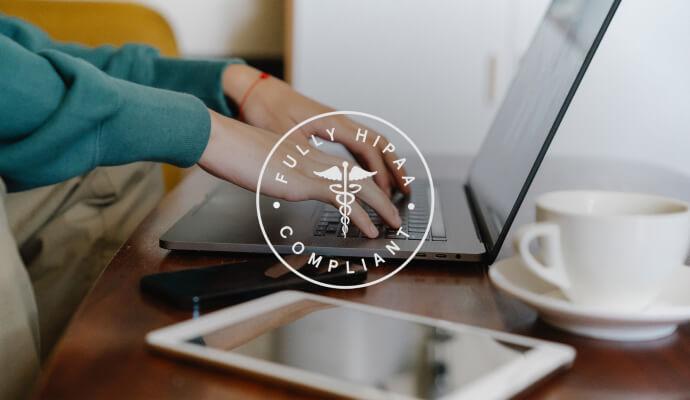A person is using a laptop on a table. Over the image is a transparent seal of HIPAA compliance.