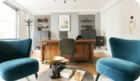A modern therapist office with suggestions for therapist office furniture: a wooden desk, two blue velvet chairs and a low table