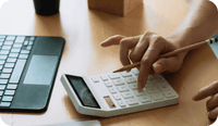 A therapist's hand types on a calculator and a laptop as they create their private practice budget