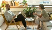 A male therapists sits in a chair as he talks with his female client who sits on a couch as they discuss the cost of therapy