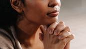 A photo of a woman holding her hands under her chin as if in prayer.