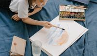 A joyful teenager sits on their bed watercolor painting. An example of art therapy activities for teenagers.