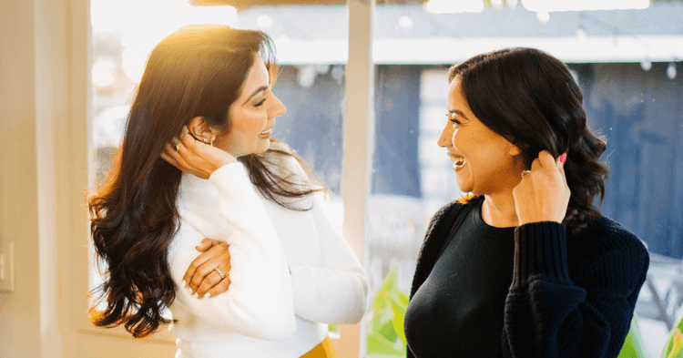 Therapists Prerna Rao and Valeri Trezise standing in a well-lit room and smiling at each other.