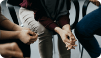 A photo of the hands and legs of people sitting in a group therapy session, as the therapist captures SOAP notes in group therapy settings and how to document for multiple clients.