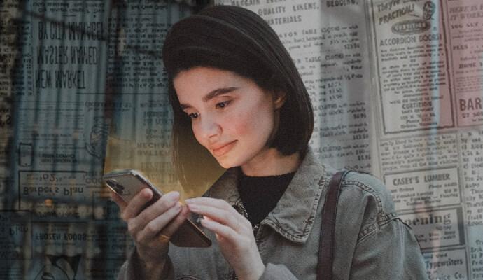 A woman is holding her phone with a faint yellow light emitting from it. She is standing in front of a collage background of newspapers.