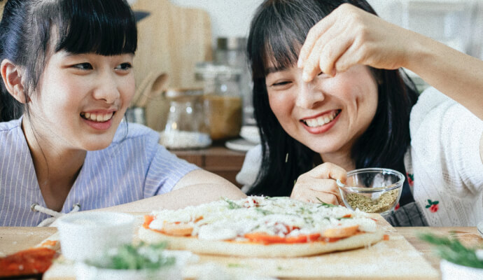 Two people are seasoning a meal together and smiling