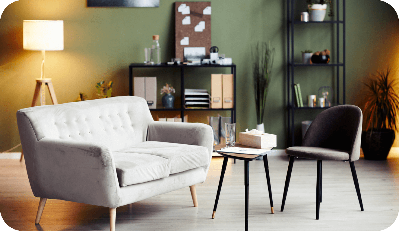 A gray modern couch and small side tables as well as a credenza are seen in a photograph of a modern therapy office with a gray rug as part of therapist design tips offered.