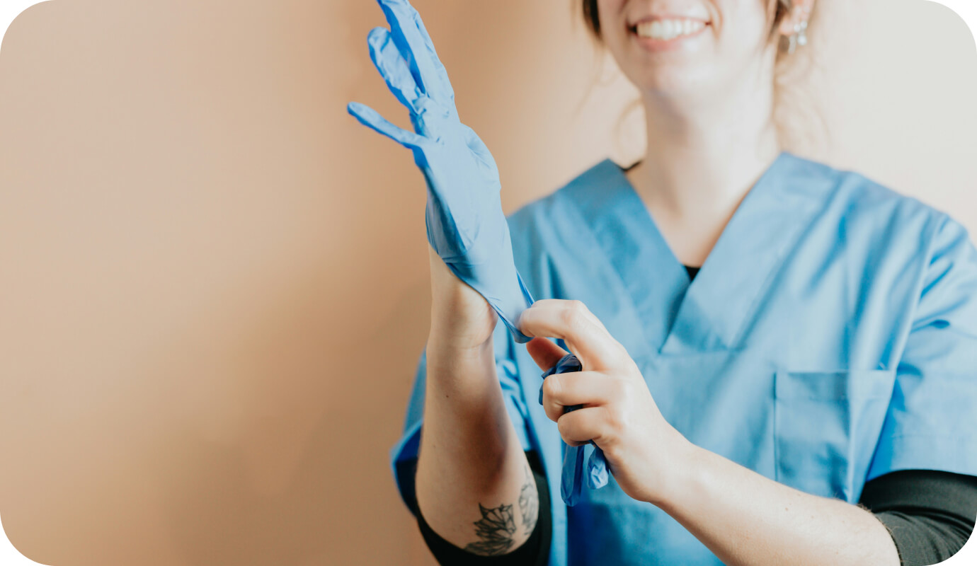 A female nurse practitioner dressed in scrubs pulls on her blue gloves and helps to address the question of "where do nurse practitioners work?"