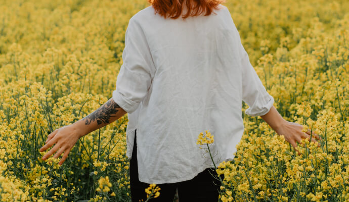 Woman outdoors in nature walking in a field of yellow flowers ponders how nature affects mental health