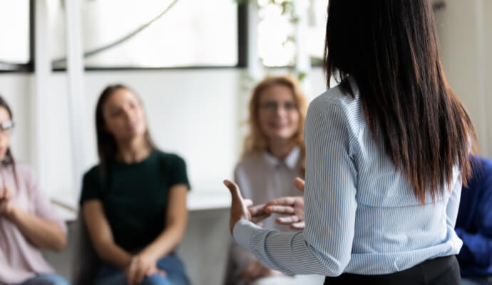 A woman is standing facing several other people, who are slightly out of focus.