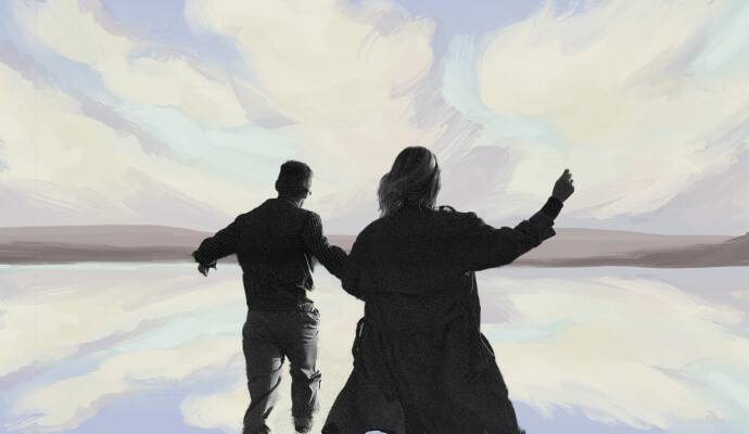 A silhouette of a couple in front of a blue, grey, and lilac sunset.