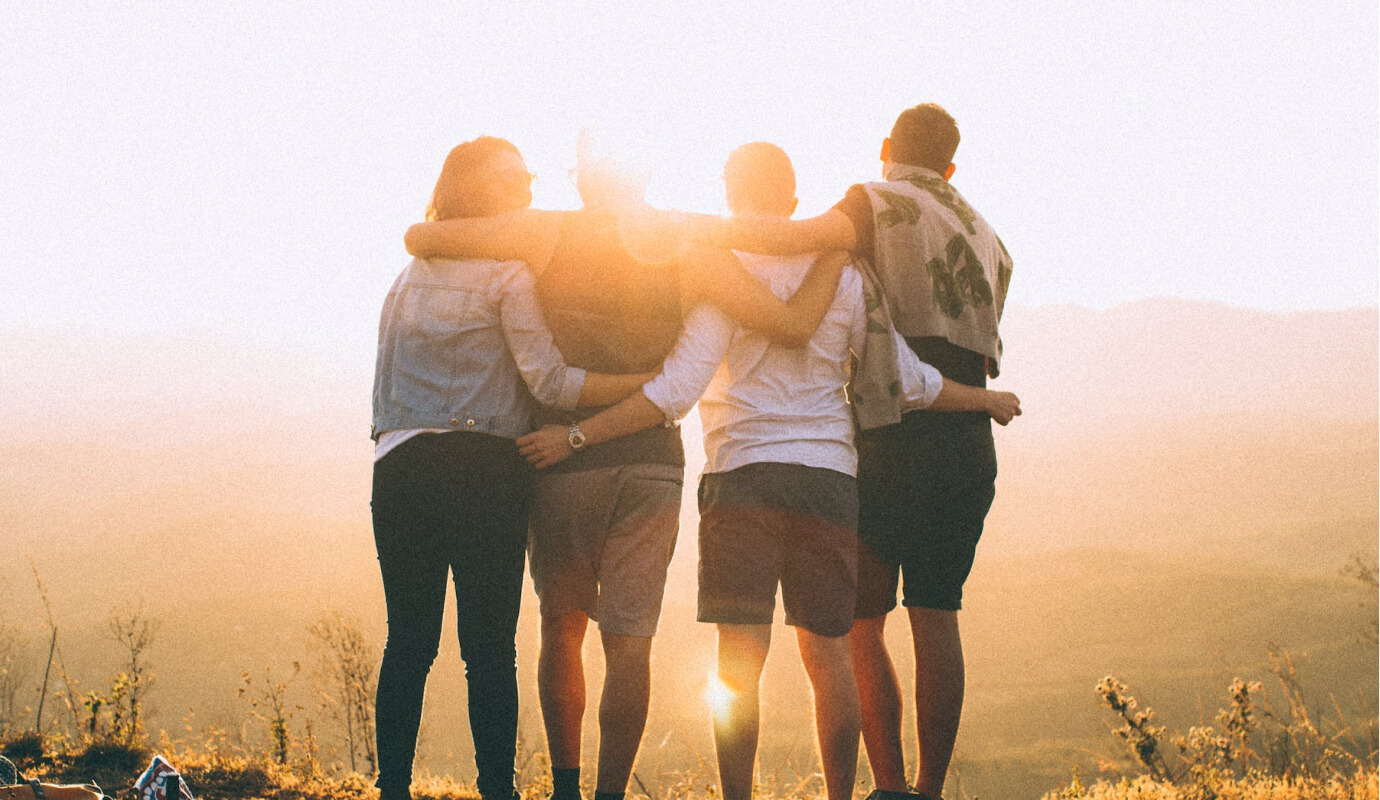 Four individuals engage in group therapy activities for adults as they stare into the sun and embrace